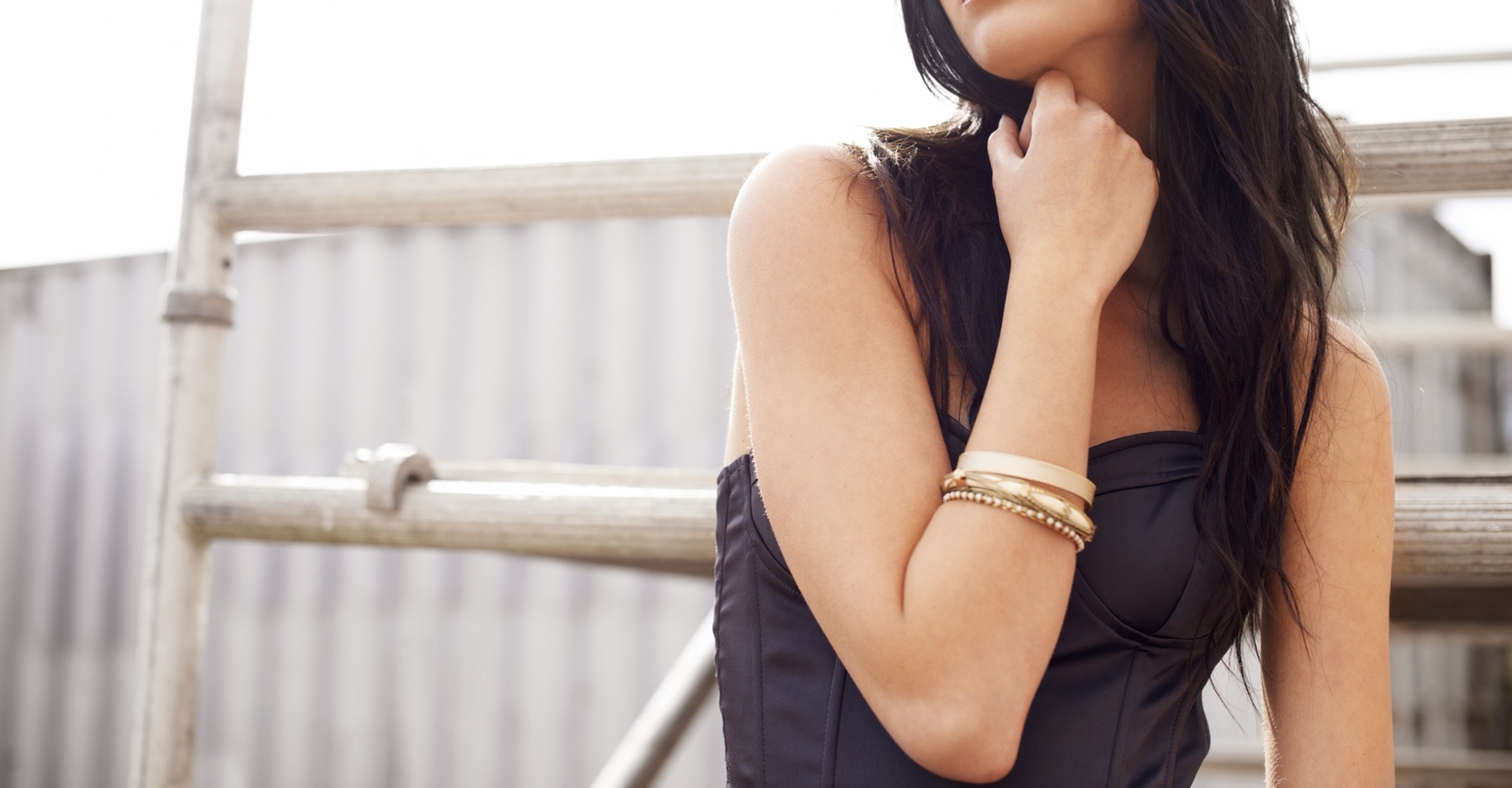 Evie in a dark dress, with gold bracelets and long dark hair.